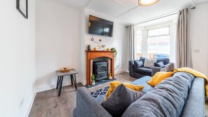 Una sala de estar moderna con chimenea, un sofá, un televisor y un ventanal con cortinas.