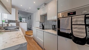 Una cocina moderna con armarios blancos, horno empotrado y refrigerador de acero inoxidable.