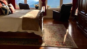 Una camera da letto con un letto, una sedia, un tappeto e vista sulle montagne attraverso una finestra.