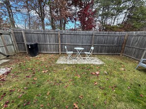 Ein Garten mit Holzzaun, einem Patio-Tisch mit Stühlen und verstreuten herabgefallenen Blättern.