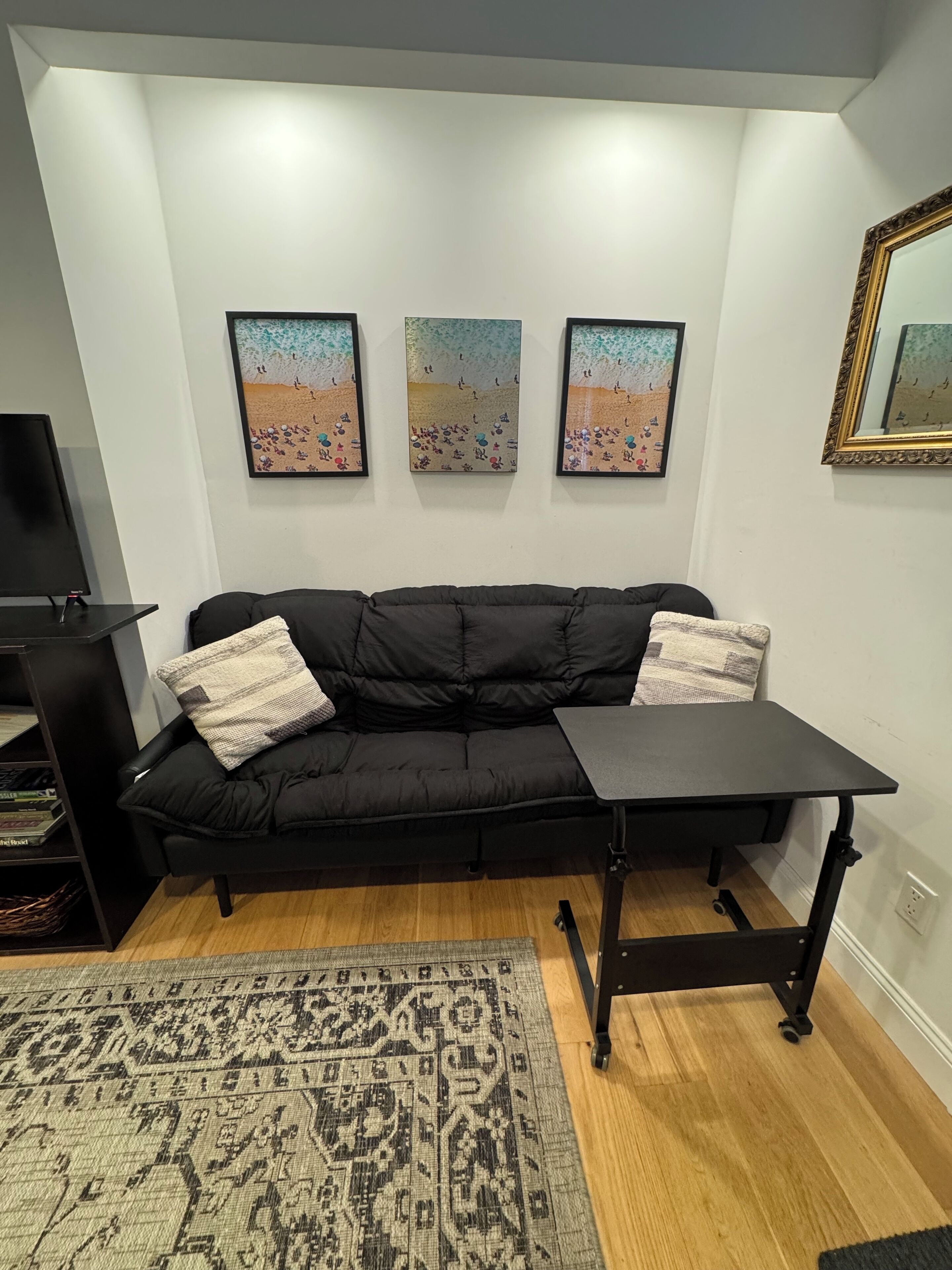 A black sofa with two pillows, a small black table, and three beach-themed wall art pieces.