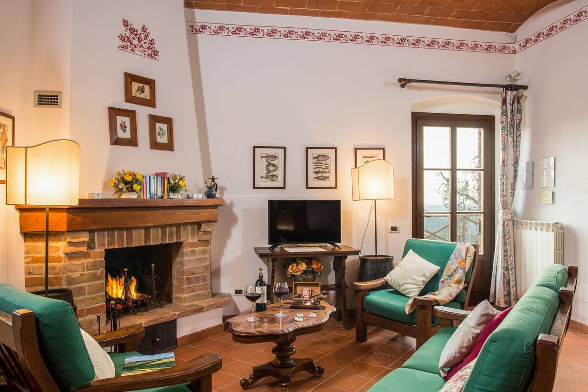 Uma sala de estar acolhedora com lareira, sofás verdes, uma televisão e quadros nas paredes.