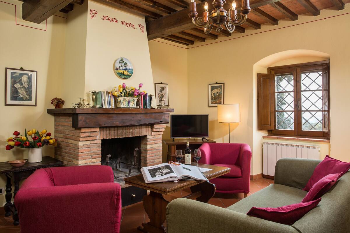 Uma sala de estar aconchegante com lareira, sofás vermelhos e verdes, uma mesa de centro de madeira e uma televisão.