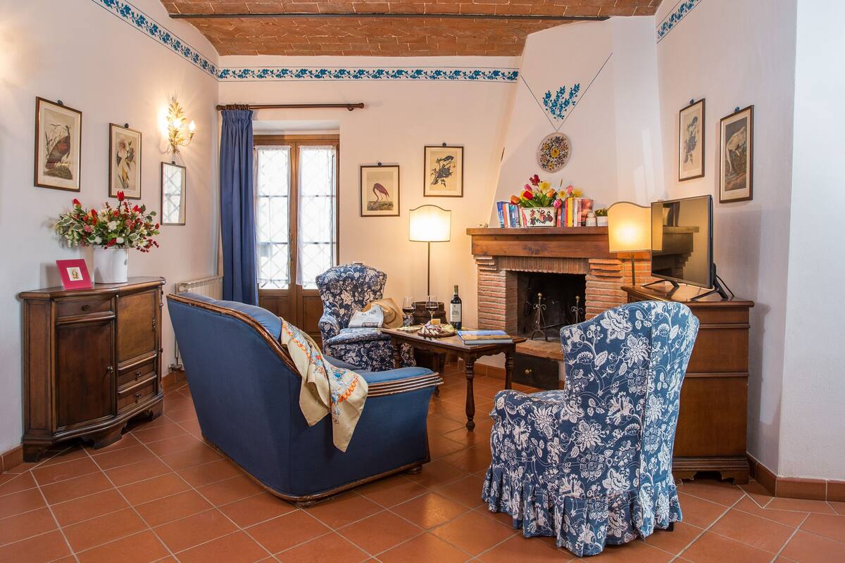 Uma sala de estar aconchegante com um sofá azul, uma poltrona estampada, uma lareira e uma estante de livros.