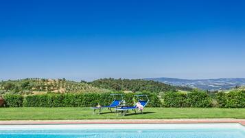 Une piscine avec deux chaises longues et une vue sur un paysage vallonné.