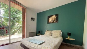 Quarto com cama, duas mesas de cabeceira, janela com vista para o verde e um quadro na parede.