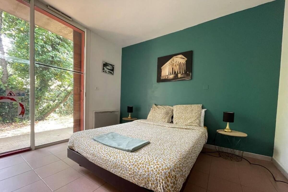 Une chambre à coucher comprenant un lit, deux tables de chevet, une fenêtre donnant sur un paysage verdoyant et un tableau accroché au mur.