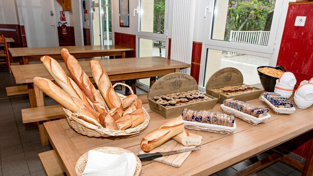 Exposição de pães e doces numa padaria, sobre mesas de madeira.
