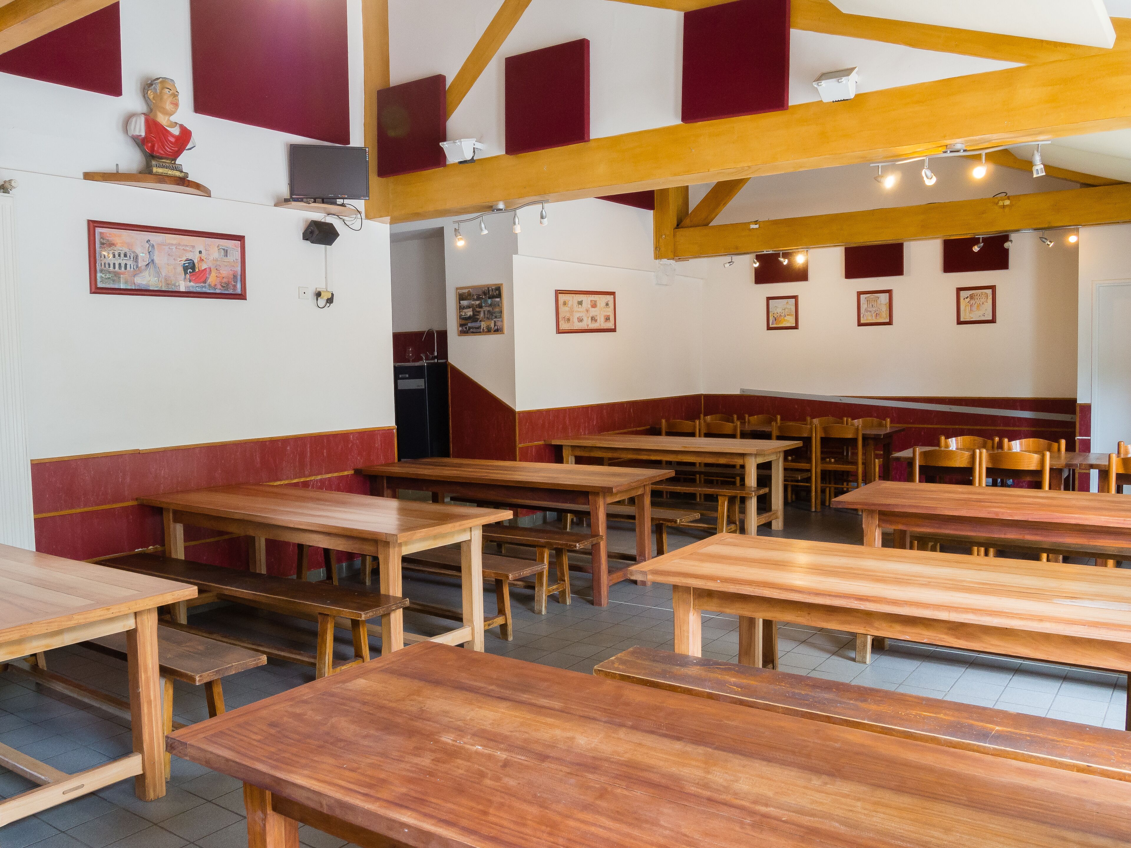 A dining area with wooden tables and benches, red and white walls, and framed pictures on the walls.