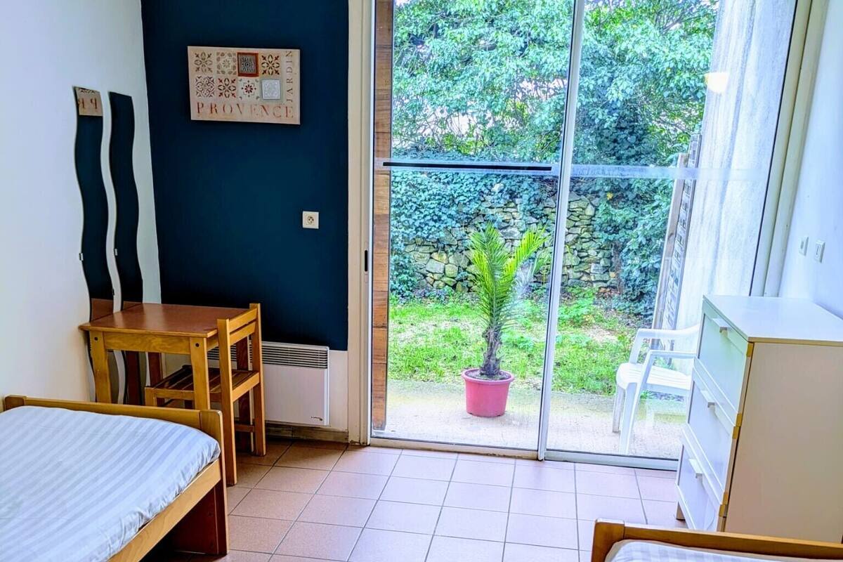 Une chambre avec deux lits, une petite table, une chaise et une plante en pot.