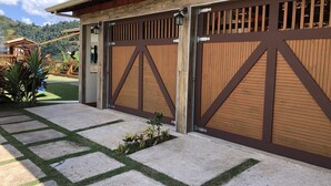 Garagem com painéis de madeira e dobradiças metálicas, caminho de concreto com grama, e cerca de madeira ao fundo.