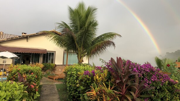 Uma casa com jardim, palmeira e um arco-íris.