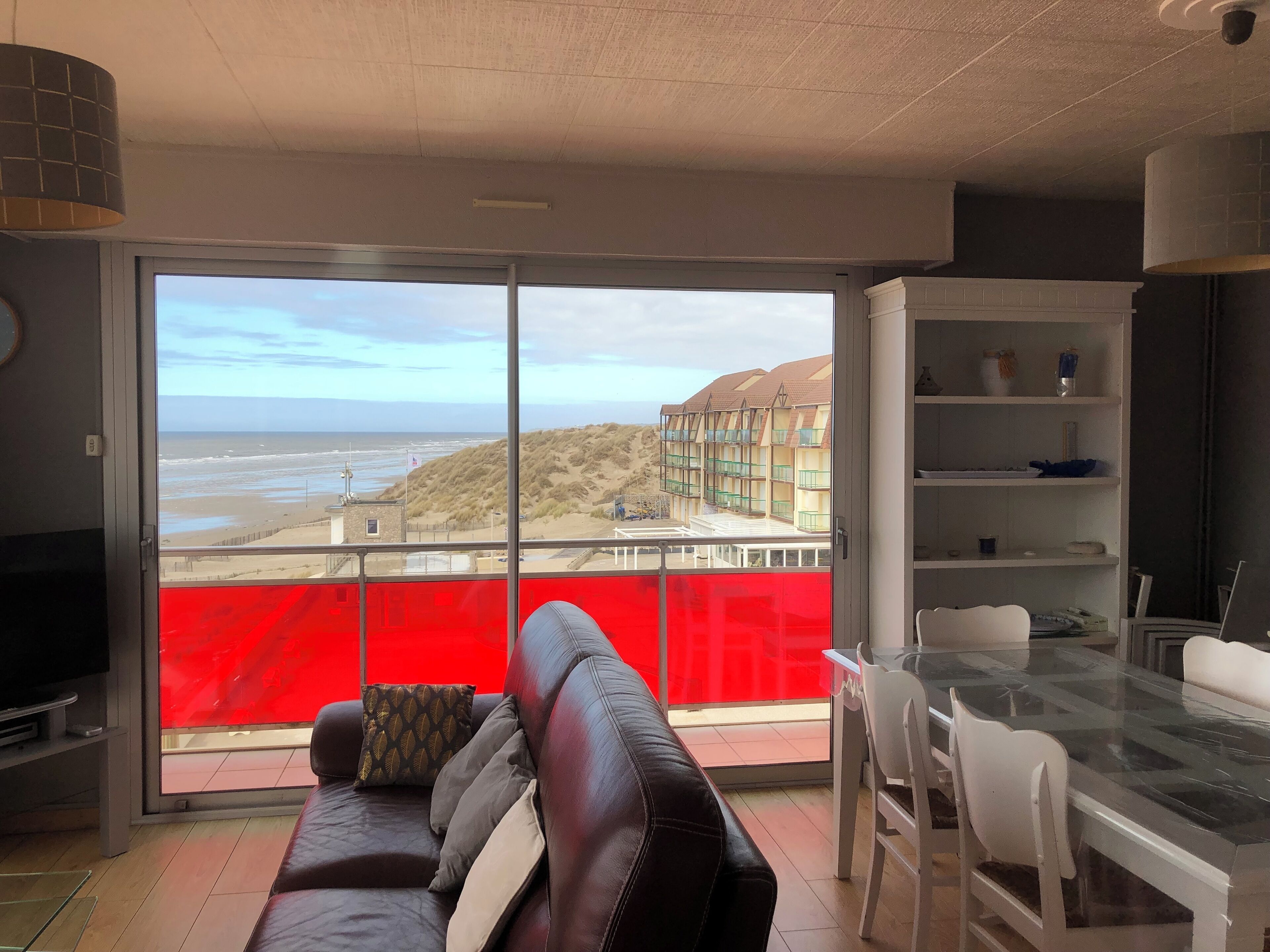 Een woonkamer met een grote schuifglazen deur naar een balkon met uitzicht op het strand en de zee.