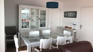 A dining area with a glass-top table, white chairs, a white cabinet with glass doors, a blue pendant light, and a framed picture on the wall. - LES BALCONS ROUGES Face Mer - Impressive sea view (SAINTE CECILE)