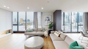 Een moderne woonkamer met grote ramen, een bank, een ronde salontafel en een plant.
