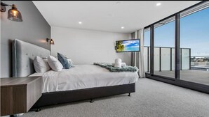 Een moderne slaapkamer met een groot bed, een televisie en een balkon met uitzicht op de stad.
