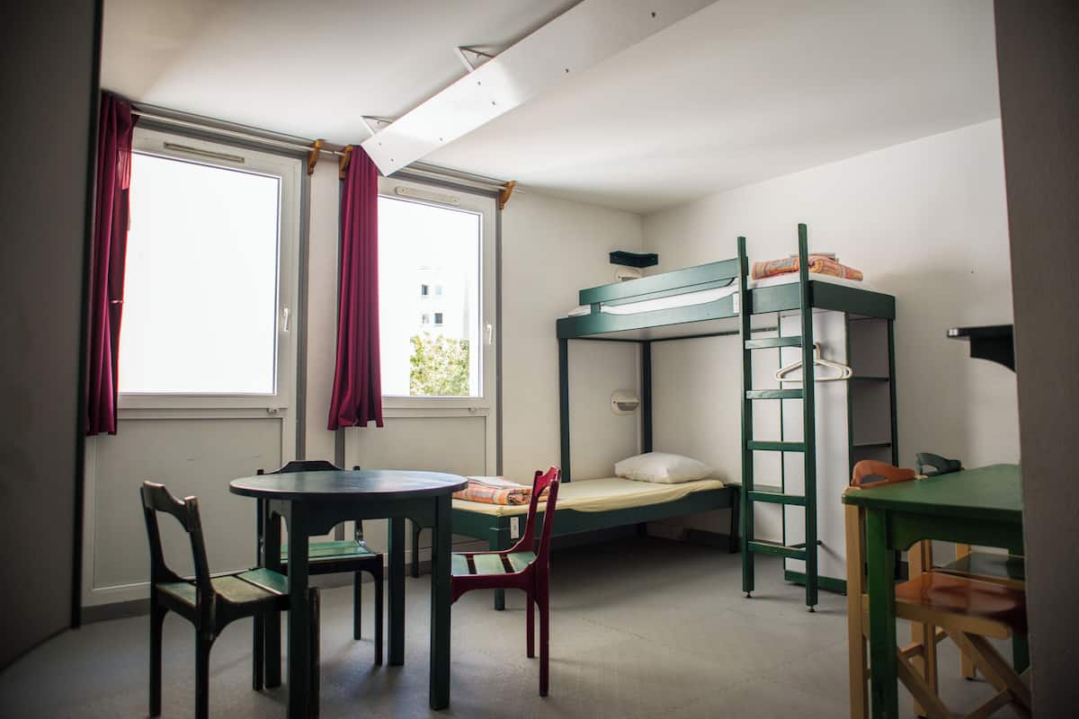 A dormitory room with bunk beds, a round table, and chairs.