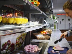 A kitchen area with a counter displaying sliced ham, a fruit basket, and a juice dispenser. - Auberge Jeunesse HI Paris - Le d’Artagnan (Paris)
