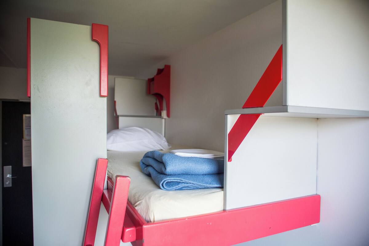 A bunk bed with a red frame, a white mattress, and a blue towel.