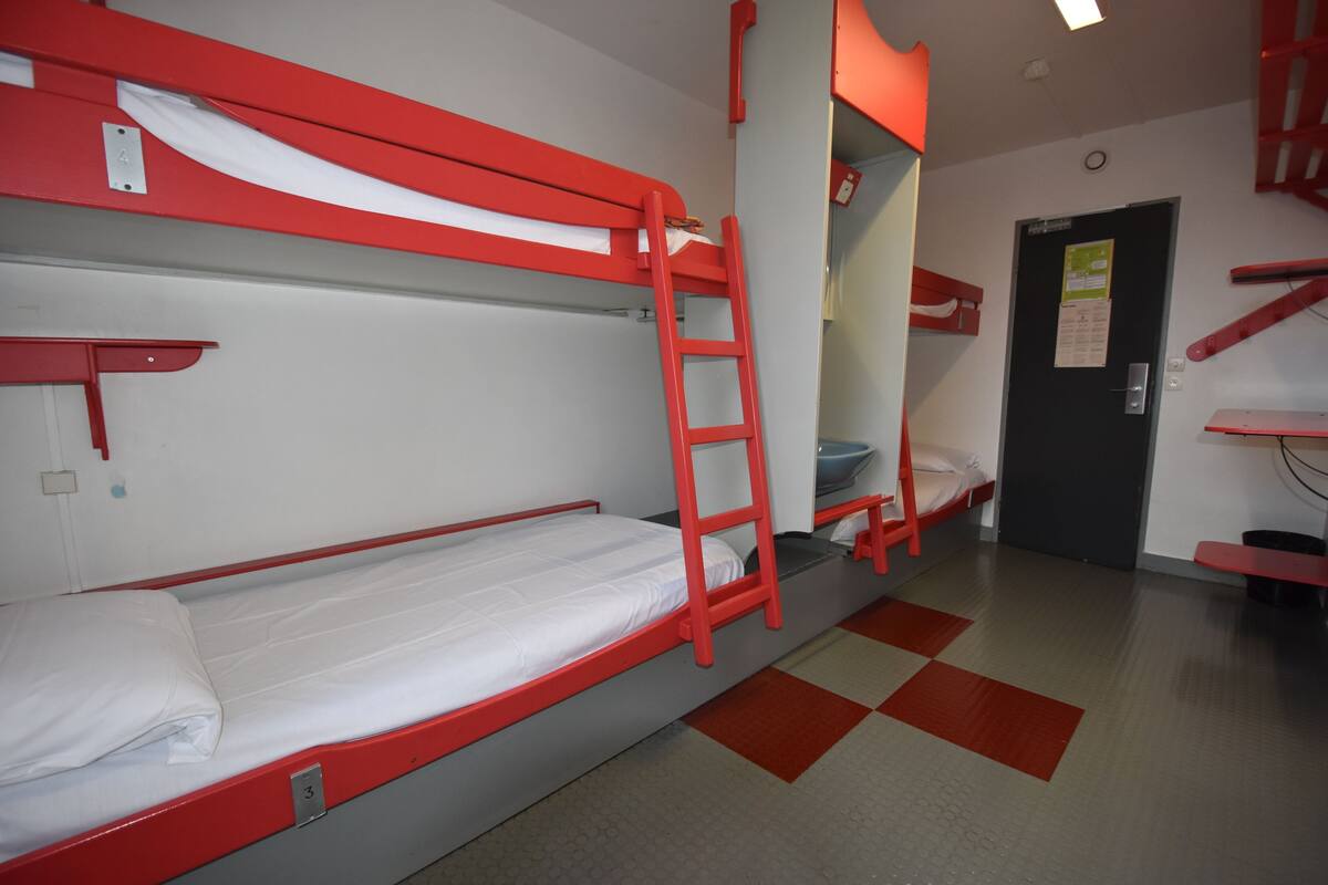 A bunk bed room with a ladder, a door with a notice, and a checkered floor.
