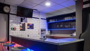A bar area with a counter, stools, a TV mounted on the wall, and shelves with glasses and bottles.