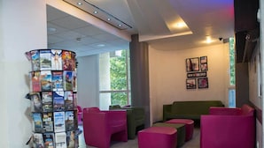 A modern lobby with a travel-themed bookcase, green and pink seating, and framed pictures on the wall.