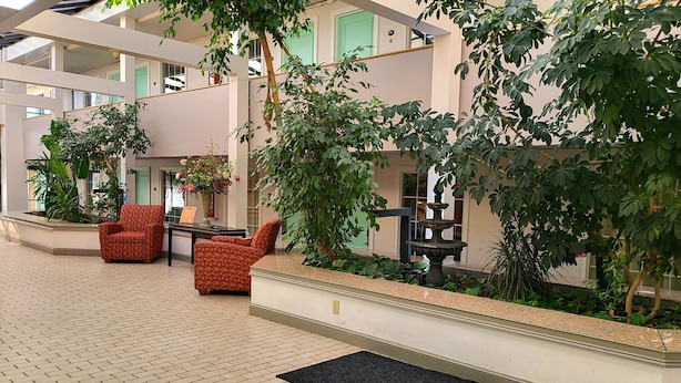 Un vaste atrium intérieur doté d’un sol carrelé, d’un espace salon avec des fauteuils à motifs et d’une végétation luxuriante comprenant des arbres et des plantes en pot.