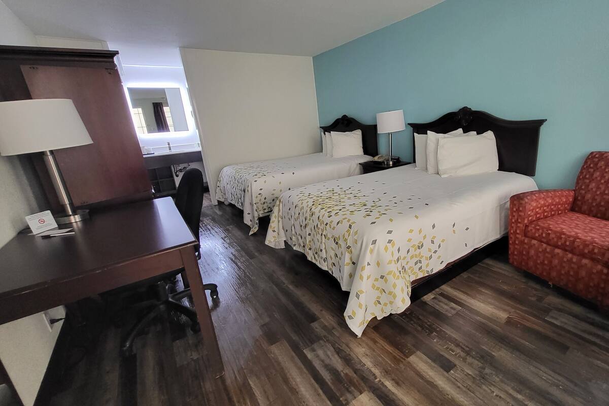 A hotel room with two beds, a desk, a chair, and a radiator.