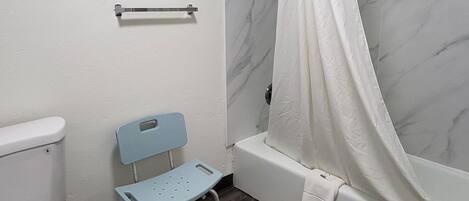 A bathroom with a toilet, a shower with a curtain, a small blue chair, and a towel rack.