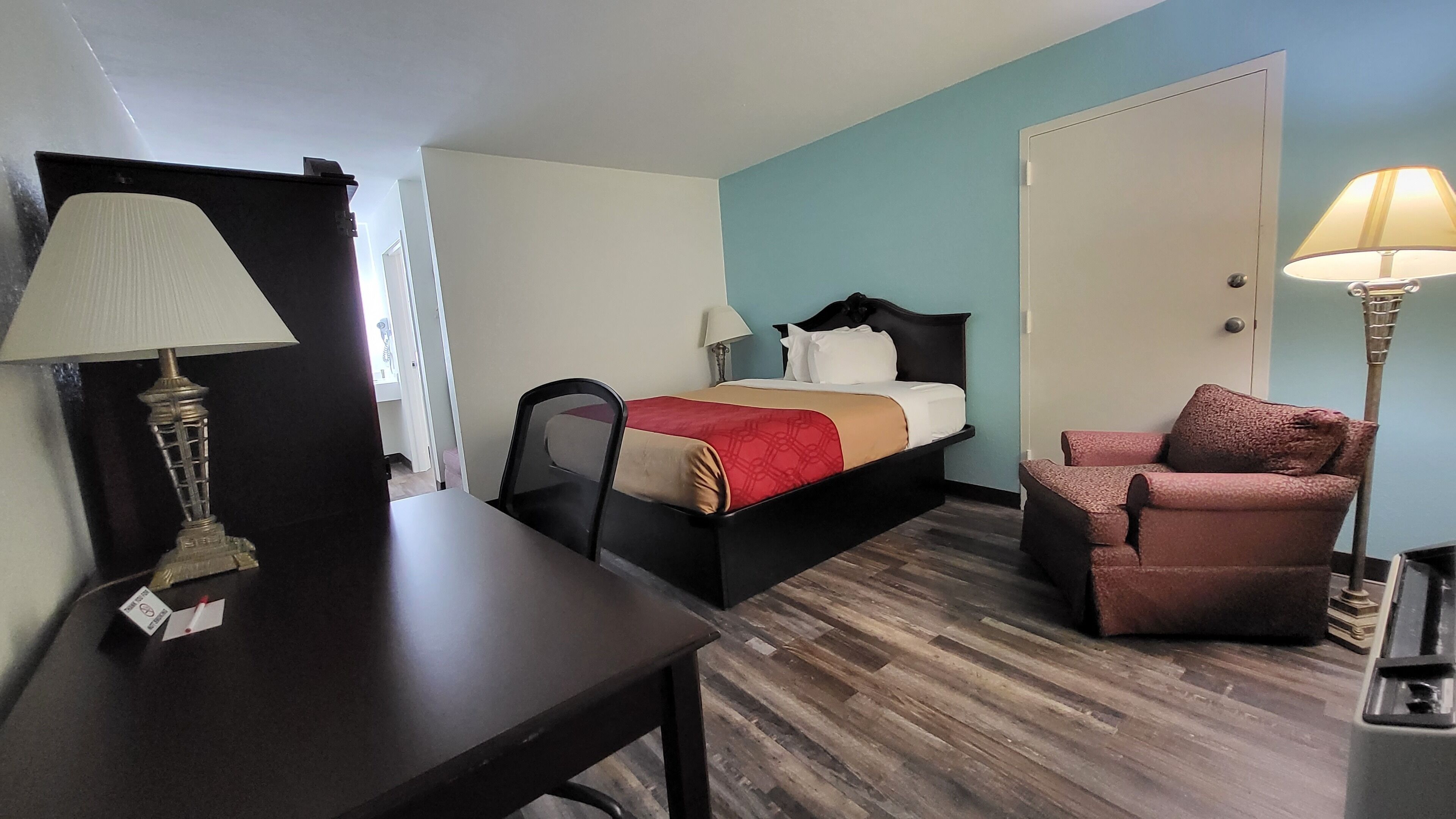 Una habitación de hotel con cama, escritorio, silla, lámpara y puerta.