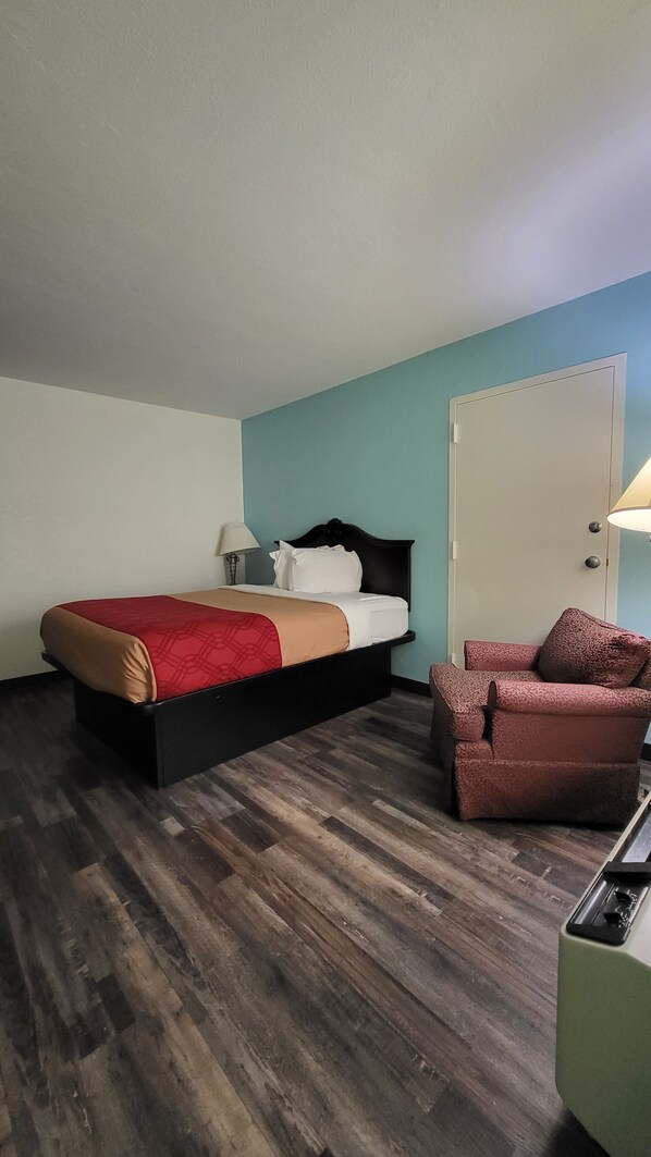 A hotel room with a bed, a chair, a desk, and a door.