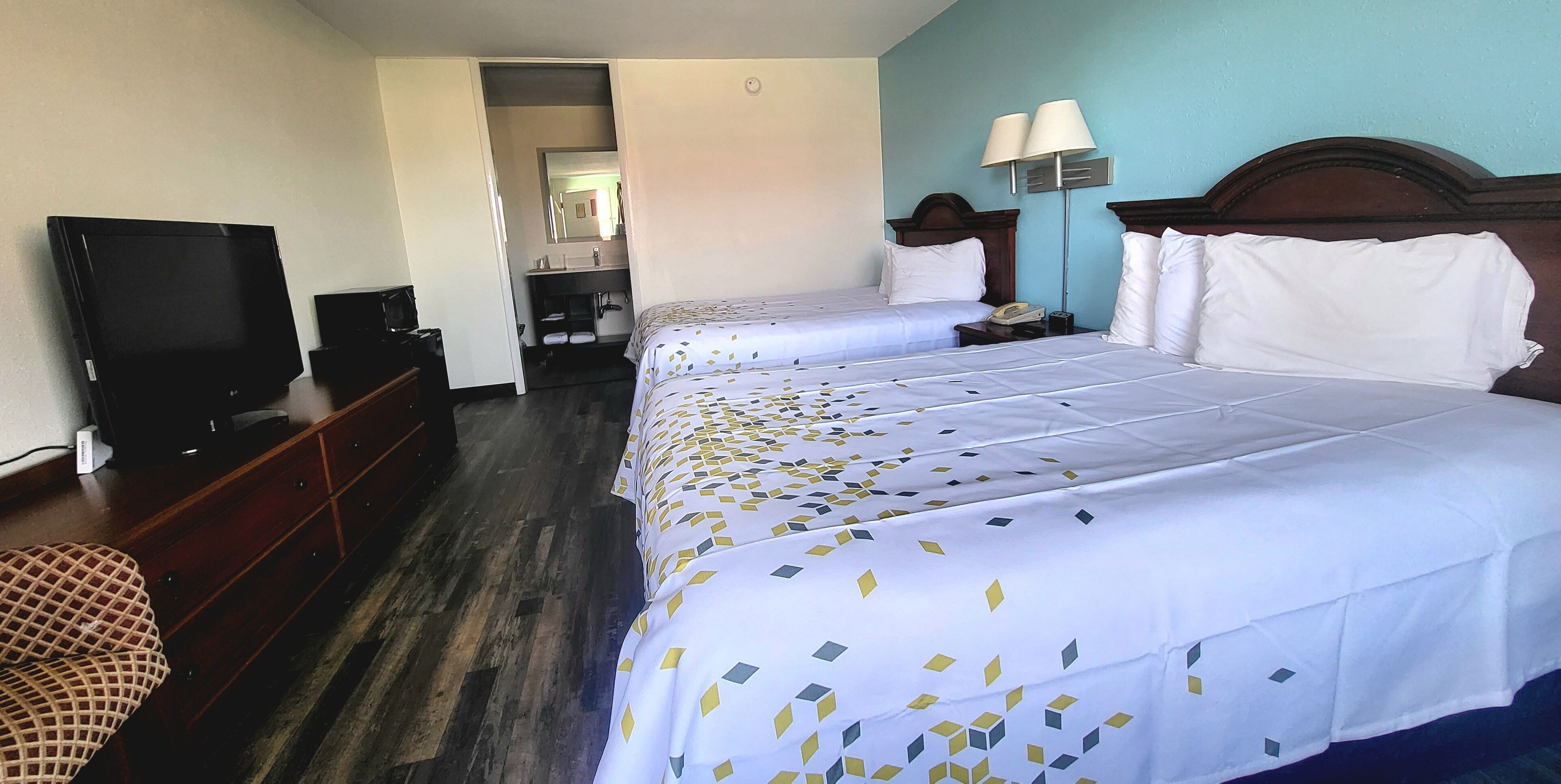 A hotel room with two beds, a television, a dresser, and a bathroom visible through an open door.