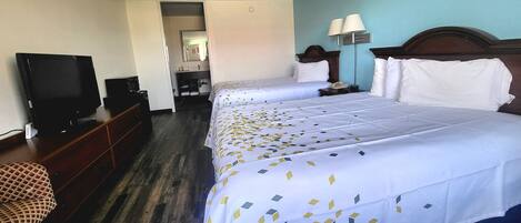 A hotel room with two beds, a television, a dresser, and a bathroom visible through an open door.