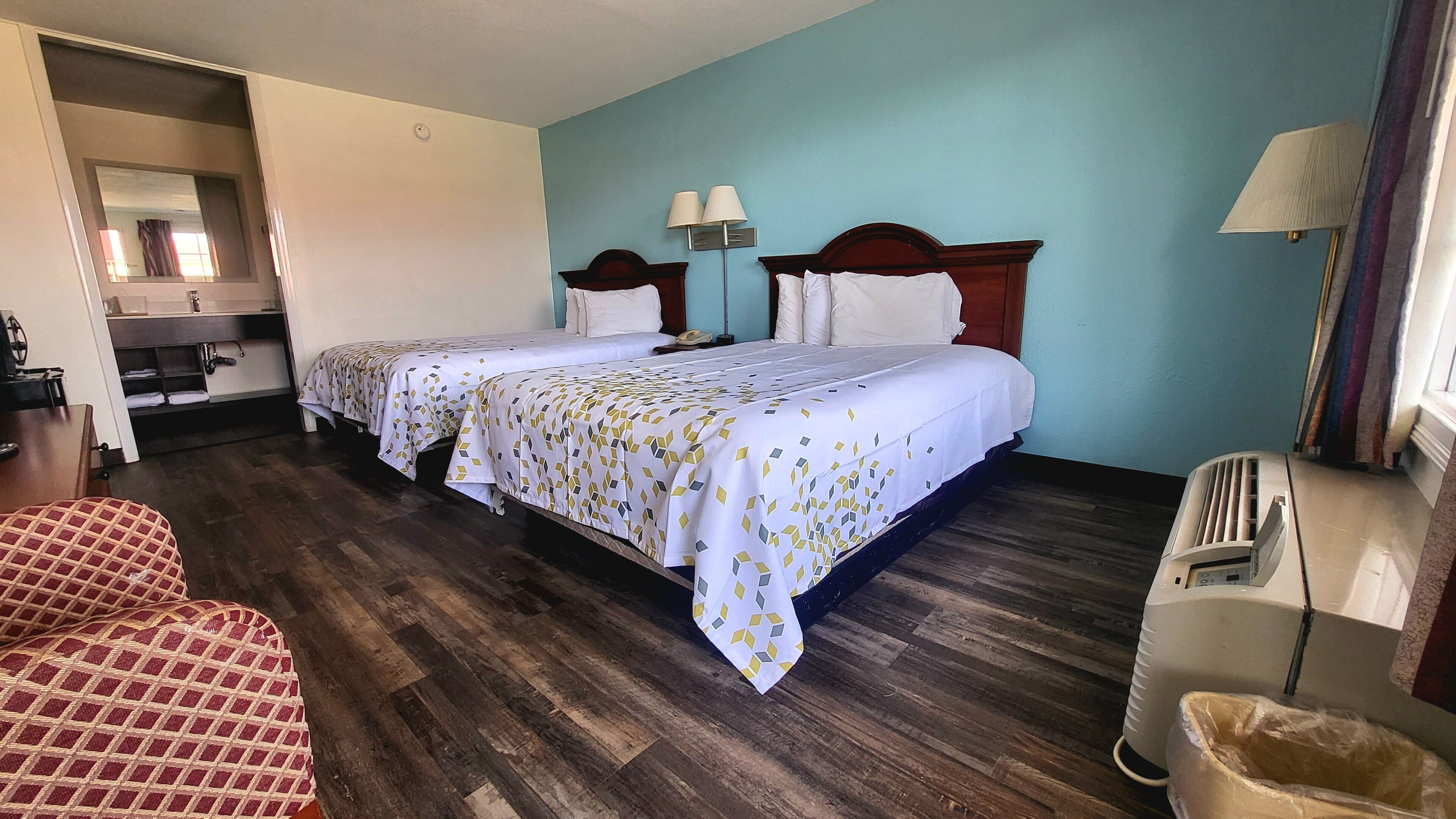 A hotel room with two beds, a desk, a chair, and a trash bin.