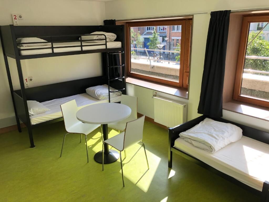 A dormitory room with bunk beds, a round table, and chairs.