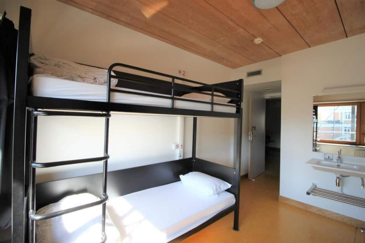 Habitación con literas, techo de madera, un lavabo y una puerta que da a otra habitación.