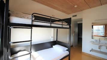 Habitación con literas, techo de madera, un lavabo y una puerta que da a otra habitación.