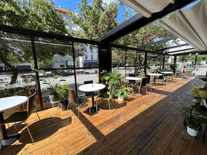 Un patio exterior con suelo de madera, mesas, sillas y plantas en macetas.