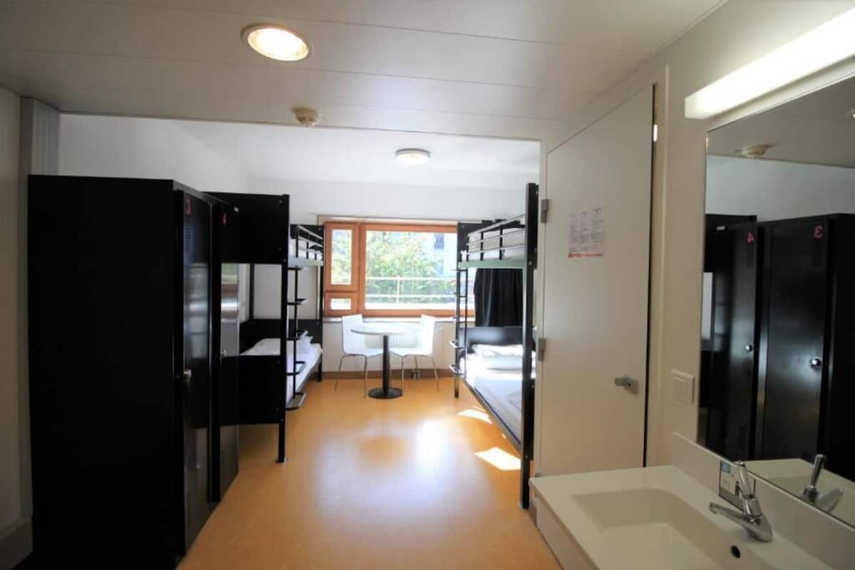 Habitación de hotel con literas, una mesita, un lavamanos y una ventana con vistas.