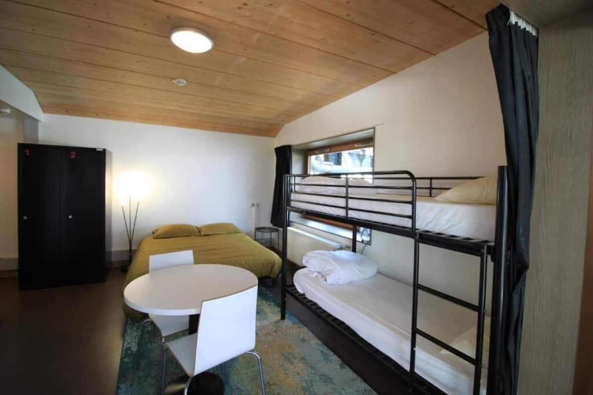 Habitación con literas, una mesa redonda y una cama con una colcha amarilla.