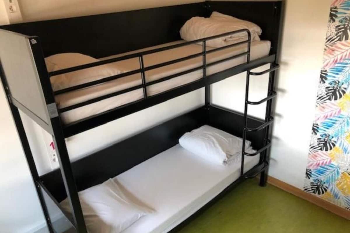 Una cama litera con tres niveles, un piso cubierto de alfombra verde y una pared con cortina estampada con hojas.