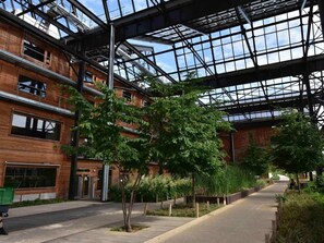 Un edificio moderno con techo de vidrio y fachada de madera, que incluye una pasarela peatonal y vegetación.