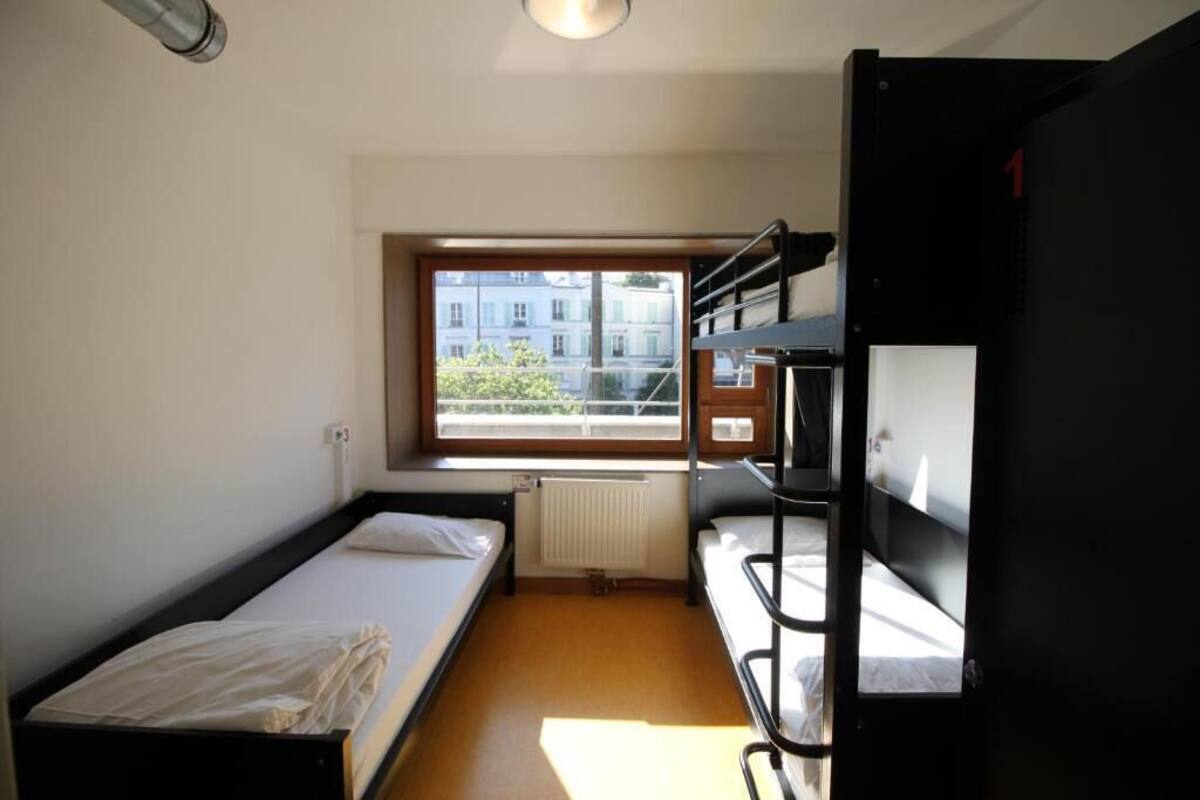 Un dormitorio con literas, una ventana con vistas a edificios y un radiador.