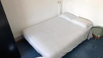 Una habitación pequeña con una cama individual, alfombra azul, ropa de cama blanca y una mesita de noche verde.