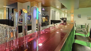Zona de bar con una barra larga, varias cañas y un área de asientos con sillas.
