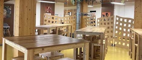 Ein Raum mit mehreren Holztischen und -stühlen, einem gelben Boden und einer Decke mit hängenden Pflanzen.