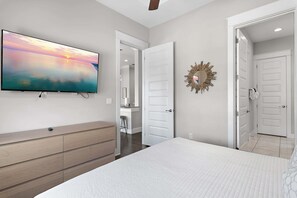 A bedroom with a bed, a TV, a dresser, and a door leading to another room. - Beach | Bikes | Great Location | Amazing Pools (Santa Rosa Beach)