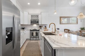 A modern kitchen with white cabinetry, stainless steel appliances, a marble countertop, and a hanging light fixture.
