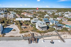 A coastal residential area with a private beach access, featuring houses with varied architecture, a sandy beach, and a wooden boardwalk.