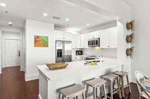 A modern kitchen with white cabinetry, a central island with stools, a refrigerator, and a microwave.